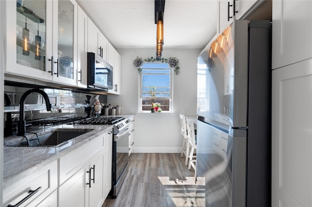 kitchen featuring light stone counters, stainless steel appliances, light wood-style floors, white cabinets, and tasteful backsplash