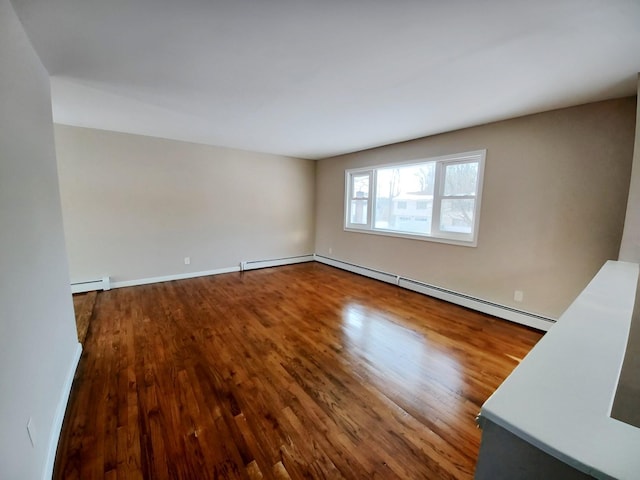 unfurnished room featuring a baseboard heating unit, baseboard heating, wood finished floors, and baseboards