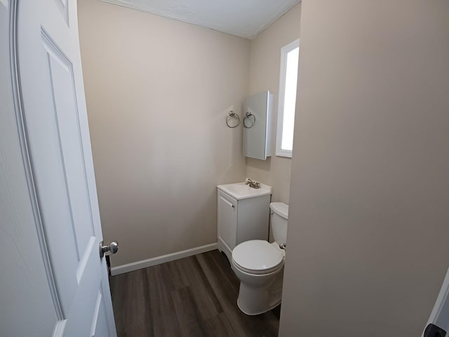 half bathroom with vanity, wood finished floors, toilet, and baseboards