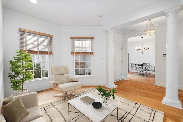 living area with light wood-type flooring, decorative columns, a notable chandelier, and baseboards