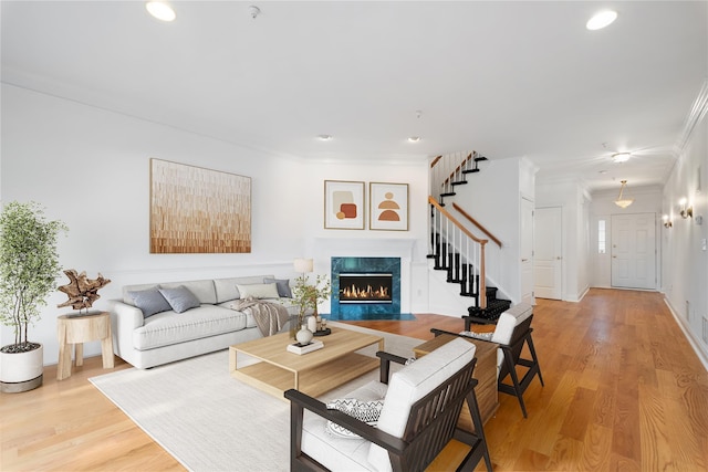 living area with ornamental molding, light wood-type flooring, a fireplace, recessed lighting, and stairs