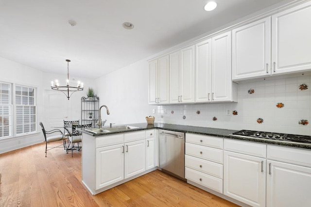 kitchen featuring a peninsula, white cabinets, a chandelier, appliances with stainless steel finishes, and a sink