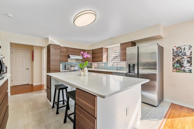 kitchen featuring tasteful backsplash, a kitchen island, appliances with stainless steel finishes, a kitchen breakfast bar, and under cabinet range hood