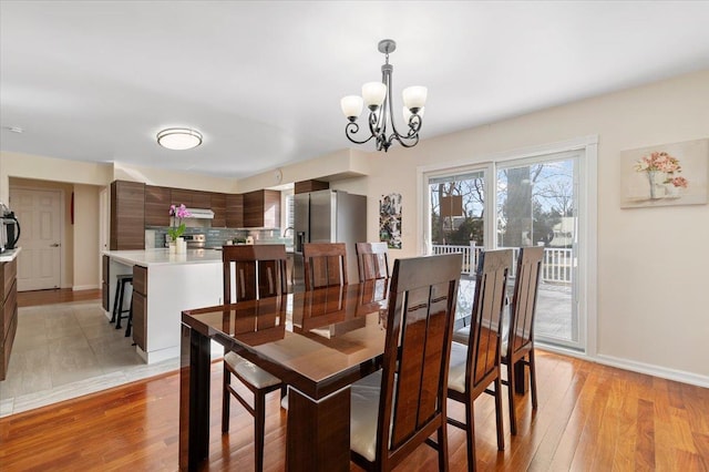 dining room with light wood-type flooring, baseboards, and a notable chandelier