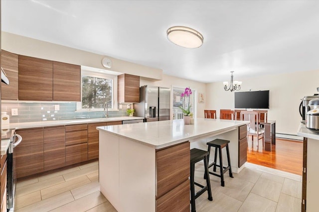 kitchen featuring brown cabinetry, stainless steel fridge with ice dispenser, a kitchen breakfast bar, a baseboard heating unit, and backsplash