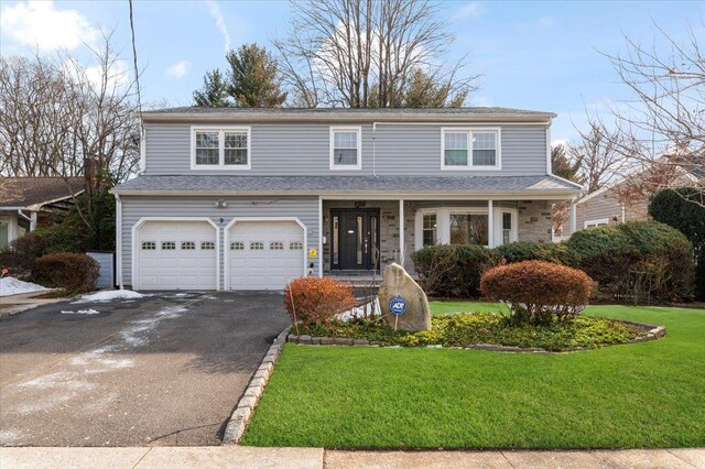 traditional-style house with roof with shingles, covered porch, an attached garage, a front yard, and driveway