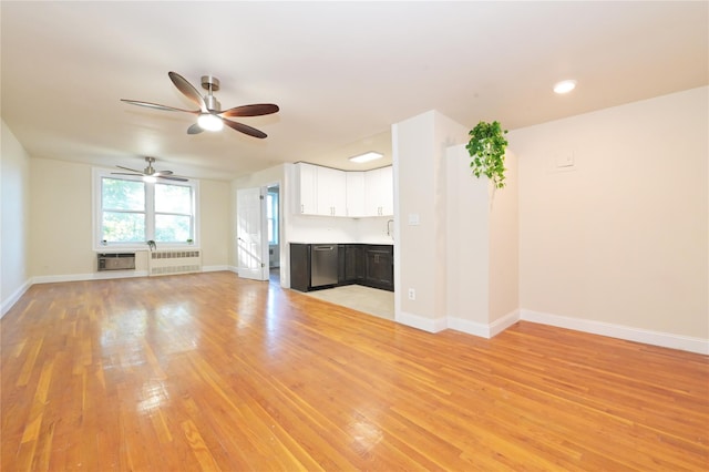 unfurnished living room with a sink, a ceiling fan, baseboards, light wood-style floors, and radiator heating unit