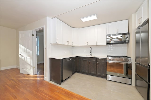 kitchen with stainless steel appliances, a sink, light countertops, and white cabinetry