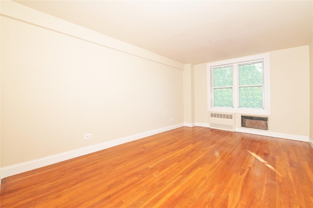 spare room with radiator, a wall unit AC, baseboards, and light wood finished floors