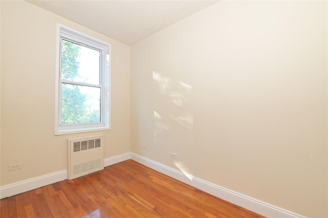 unfurnished room with baseboards, light wood finished floors, radiator heating unit, and a textured ceiling