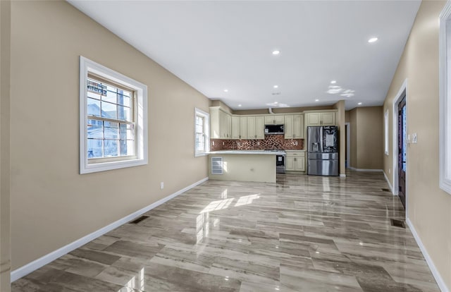 kitchen featuring appliances with stainless steel finishes, cream cabinetry, backsplash, and baseboards