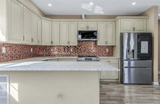 kitchen featuring tasteful backsplash, appliances with stainless steel finishes, a sink, light stone countertops, and a peninsula