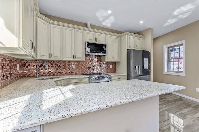 kitchen with appliances with stainless steel finishes, a sink, light stone countertops, and tasteful backsplash