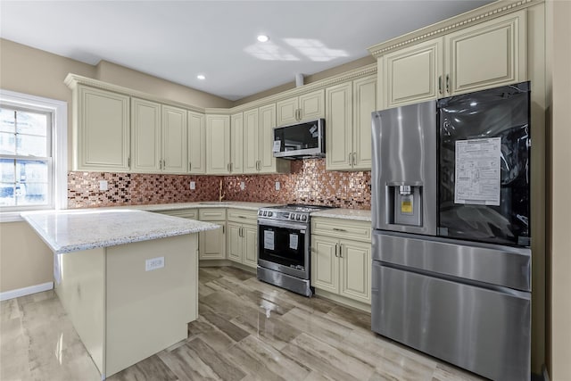 kitchen featuring appliances with stainless steel finishes, cream cabinetry, backsplash, and light stone countertops