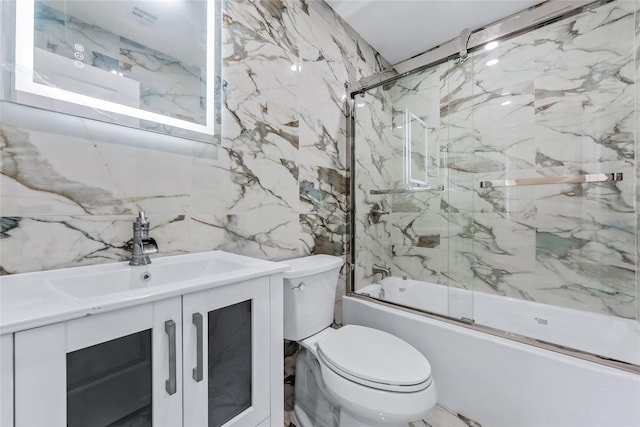 bathroom featuring stone wall, bath / shower combo with glass door, vanity, and toilet