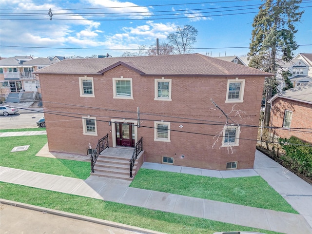 view of front of house featuring brick siding, fence, a front lawn, and roof with shingles