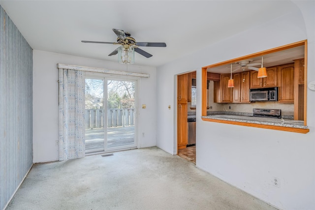 kitchen featuring pendant lighting, brown cabinets, light colored carpet, appliances with stainless steel finishes, and a ceiling fan