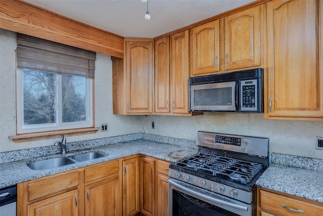 kitchen with light stone countertops, stainless steel appliances, a sink, and brown cabinetry