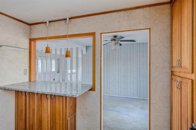 kitchen featuring brown cabinetry, a ceiling fan, light stone counters, hanging light fixtures, and crown molding