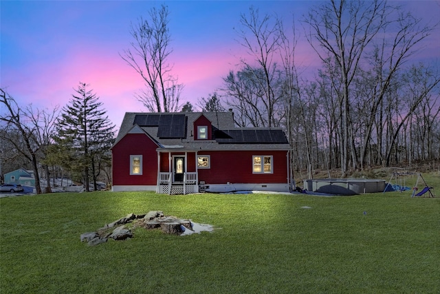 back of house at dusk with crawl space, a shingled roof, a lawn, and solar panels