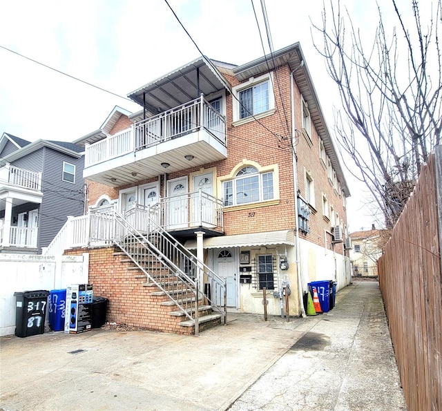 view of front facade featuring a balcony, fence, and brick siding