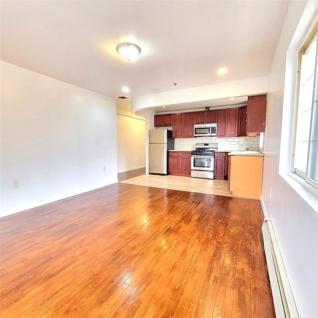 kitchen with a baseboard radiator, appliances with stainless steel finishes, light countertops, light wood-type flooring, and backsplash