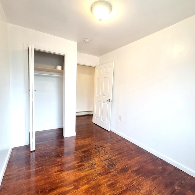 unfurnished bedroom with a closet, baseboards, baseboard heating, and wood finished floors