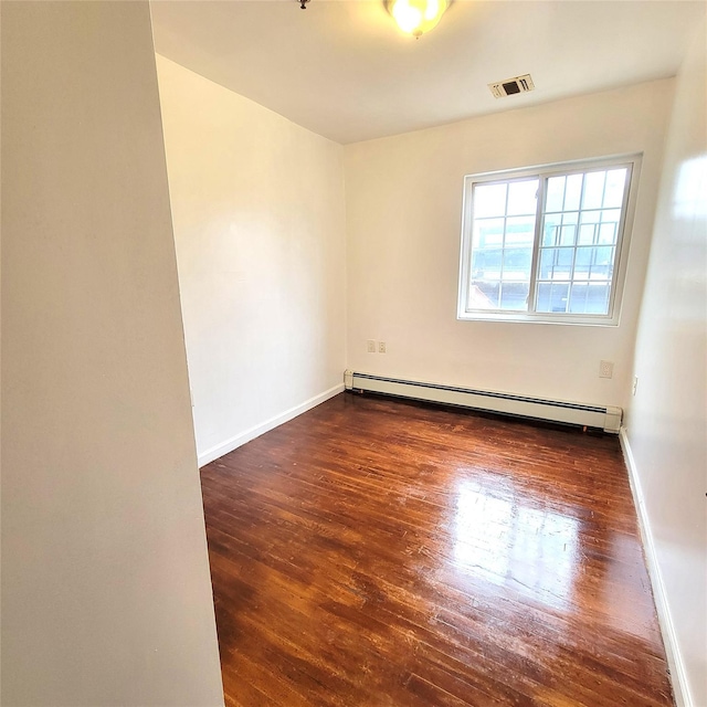 spare room with a baseboard heating unit, baseboards, visible vents, and wood finished floors