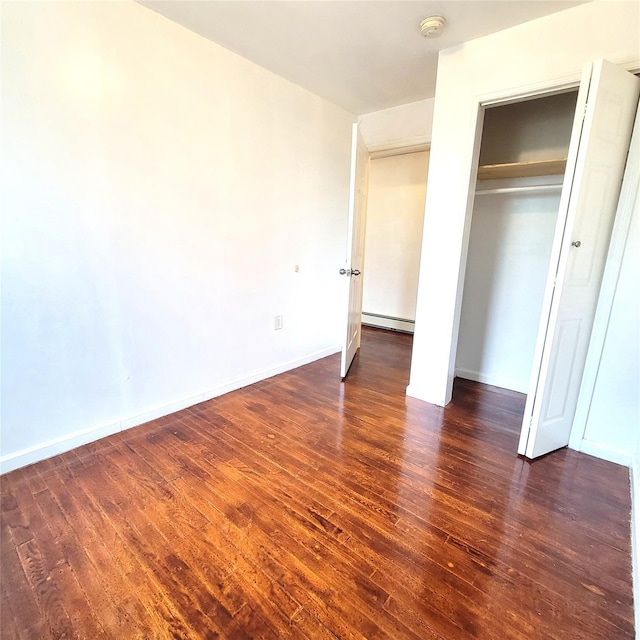 unfurnished bedroom featuring a closet, baseboards, baseboard heating, and wood finished floors