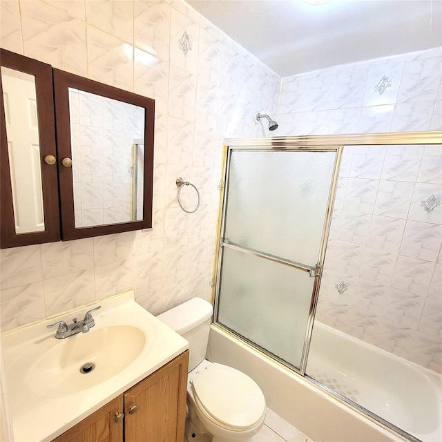 bathroom with combined bath / shower with glass door, vanity, toilet, and tile walls