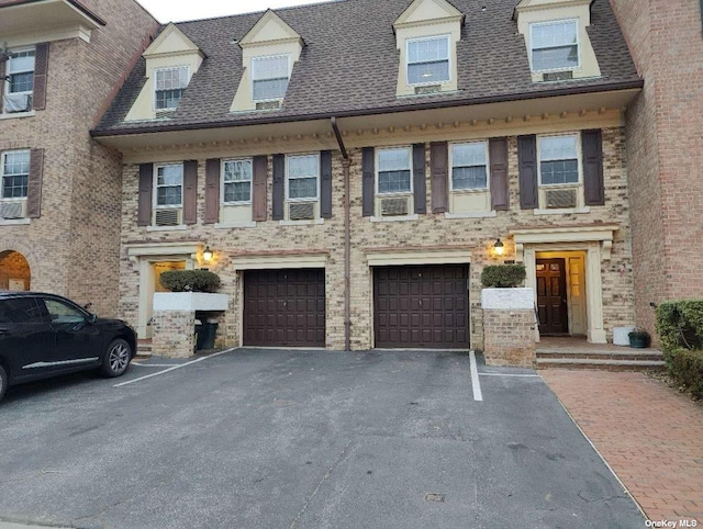 view of property featuring driveway, a shingled roof, an attached garage, and cooling unit