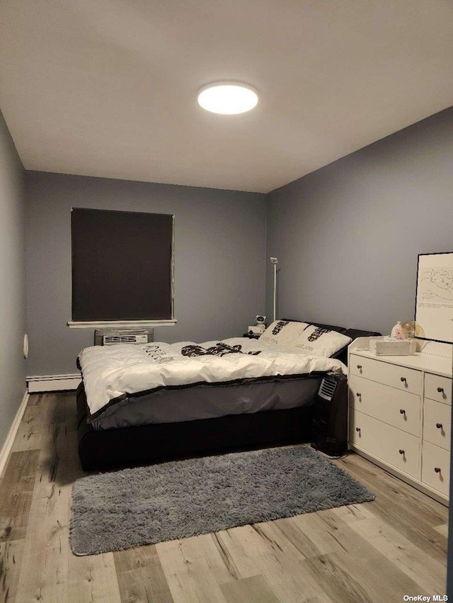 bedroom with a baseboard heating unit, an AC wall unit, light wood-type flooring, and baseboards