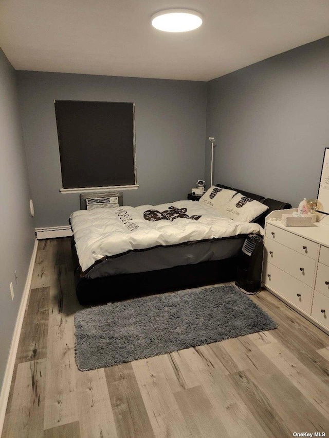 bedroom with a wall unit AC, light wood-style flooring, baseboards, and baseboard heating