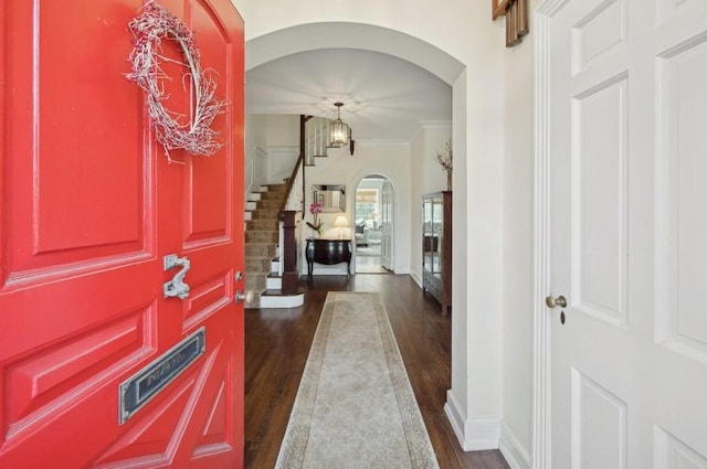 foyer entrance with baseboards, dark wood finished floors, arched walkways, ornamental molding, and stairs