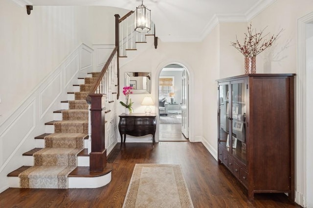 entryway featuring crown molding, a decorative wall, dark wood-style floors, and arched walkways