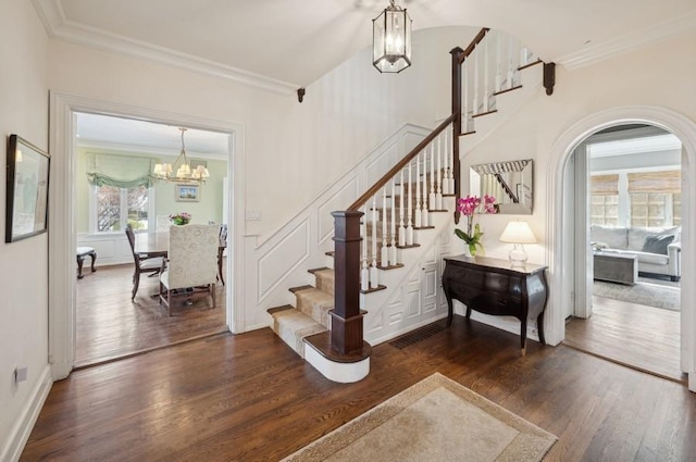 stairs featuring a chandelier, a decorative wall, crown molding, and wood finished floors