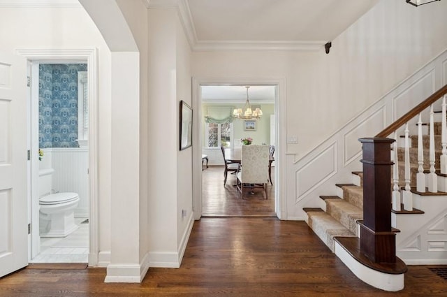 foyer entrance featuring a wainscoted wall, dark wood-style floors, crown molding, a decorative wall, and stairs