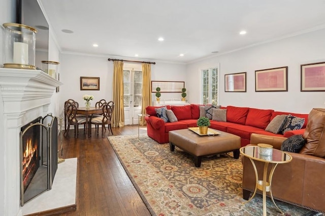 living area with recessed lighting, a warm lit fireplace, dark wood-style flooring, and crown molding