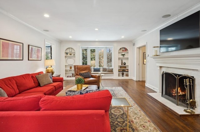 living area featuring built in shelves, a lit fireplace, wood finished floors, and crown molding