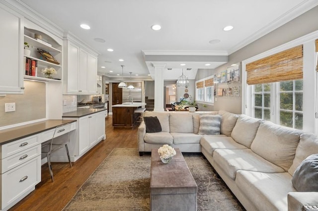 living area featuring dark wood-style floors, built in desk, recessed lighting, crown molding, and ornate columns