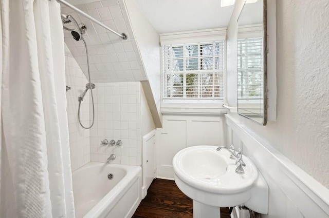 bathroom featuring wood finished floors, shower / bath combination with curtain, wainscoting, a decorative wall, and a textured wall