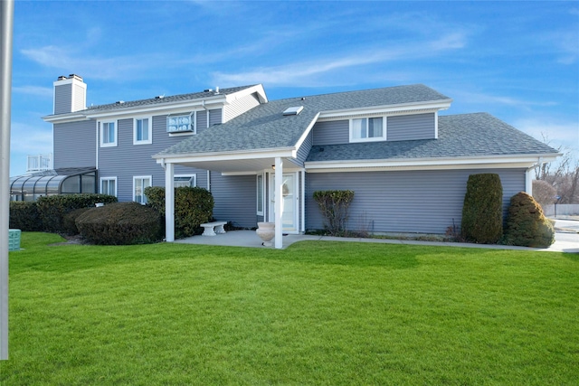 back of property with a shingled roof, a lawn, and a chimney