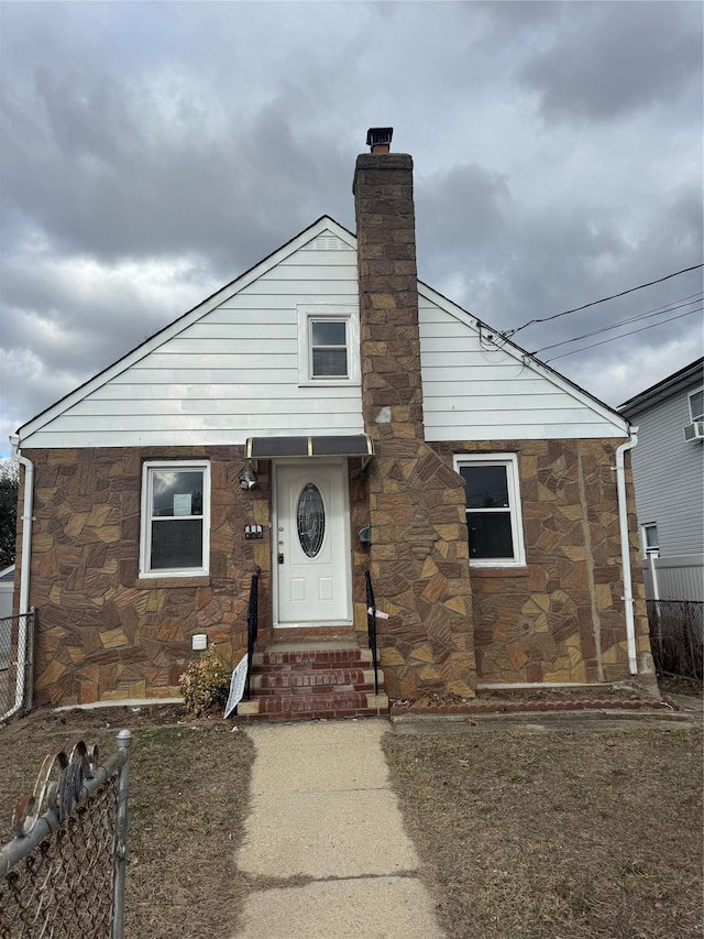 view of front of house with entry steps, stone siding, a chimney, and fence