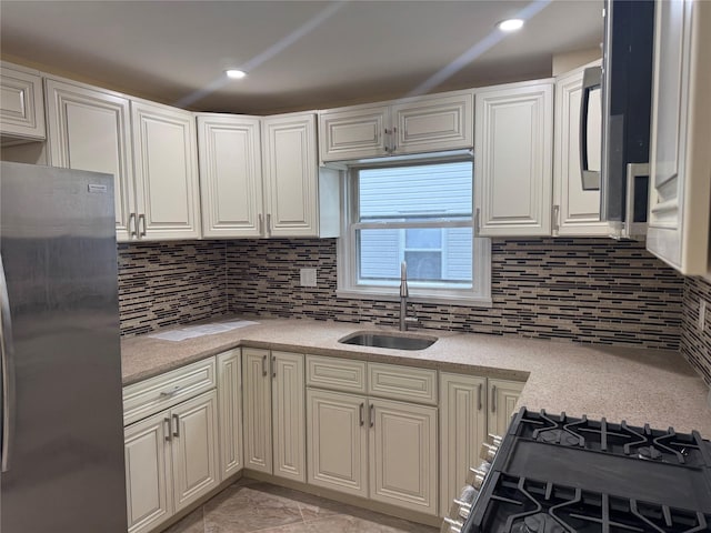 kitchen with gas range oven, light countertops, backsplash, freestanding refrigerator, and a sink