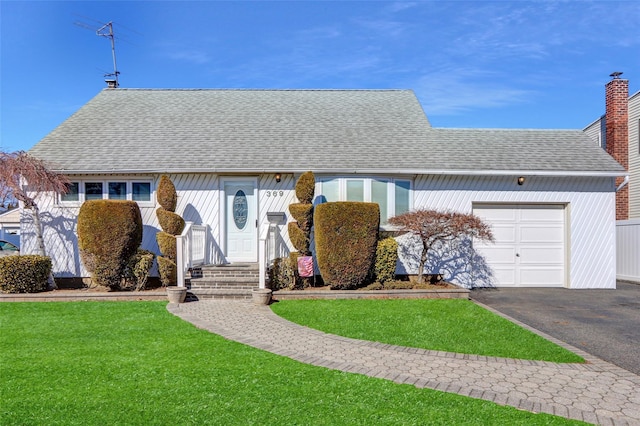 ranch-style house with aphalt driveway, a garage, roof with shingles, a front lawn, and a chimney