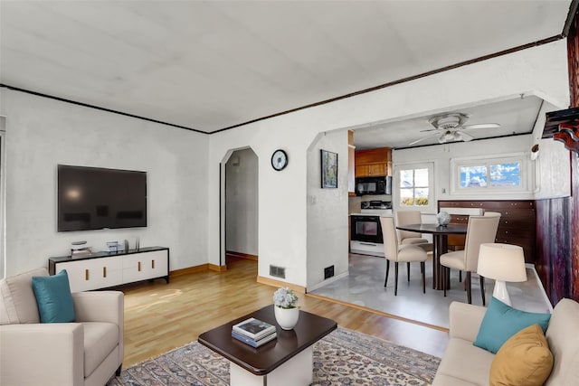 living area with arched walkways, wood finished floors, visible vents, baseboards, and a ceiling fan