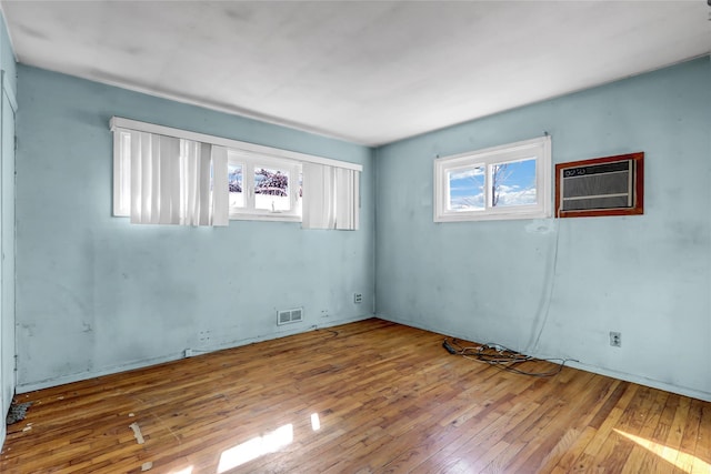 empty room with a wall unit AC, wood-type flooring, and visible vents