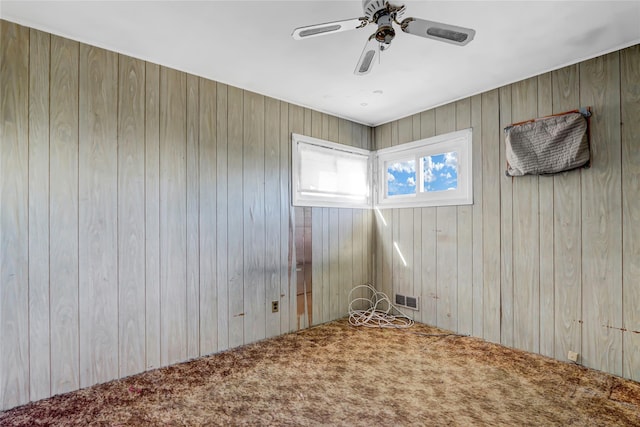 carpeted empty room featuring wooden walls, visible vents, and a ceiling fan