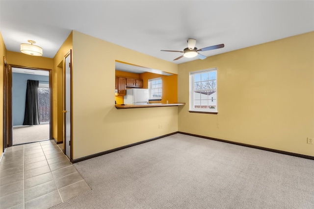 unfurnished living room with light carpet, light tile patterned floors, a ceiling fan, and baseboards