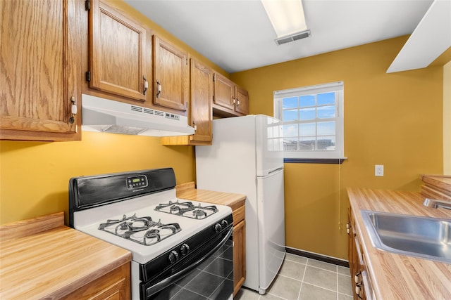 kitchen with white appliances, visible vents, under cabinet range hood, a sink, and light tile patterned flooring